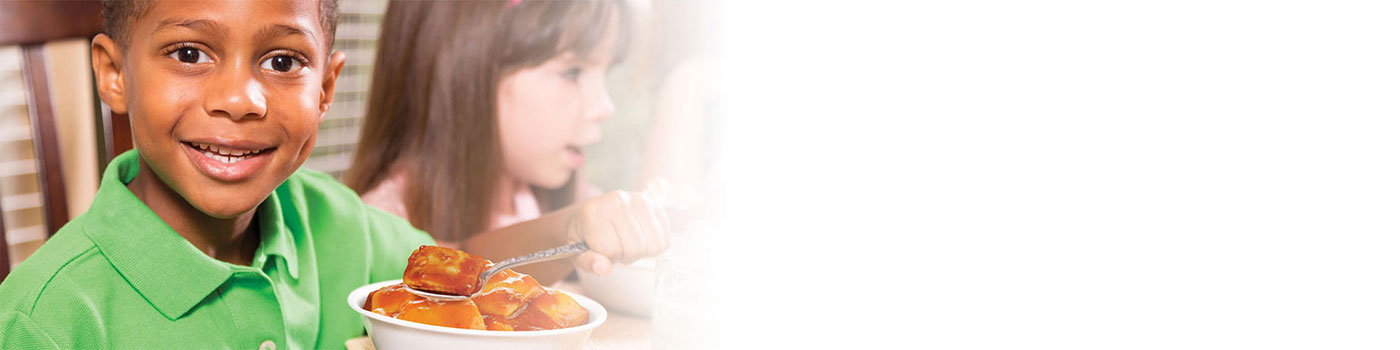 Young boy eating ravioli with young girl behind him
